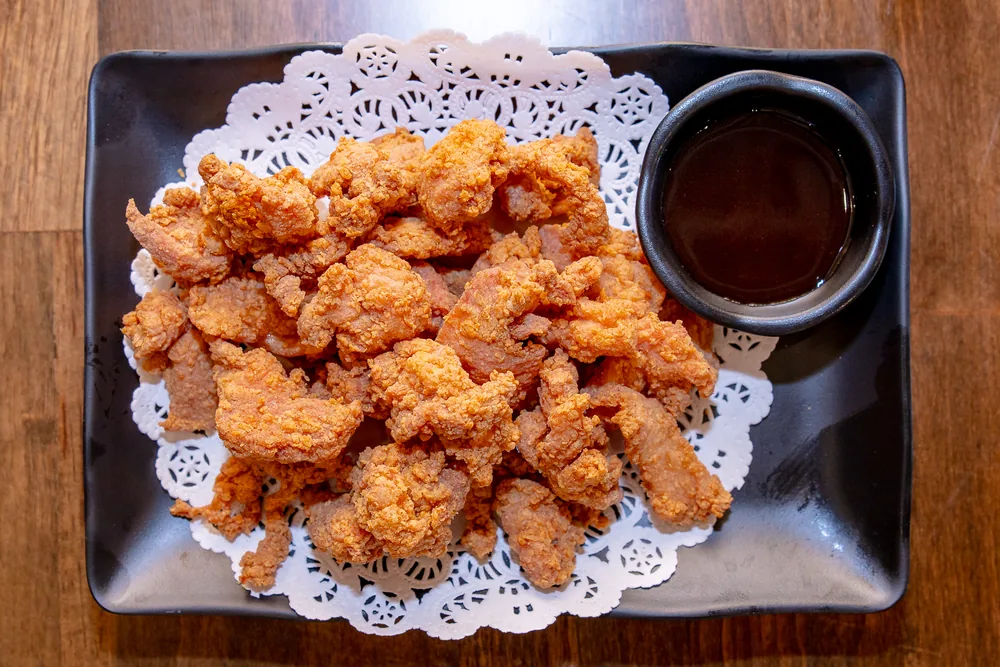 Japanese fried chicken pieces on a paper doily beside a bowl of dipping sauce