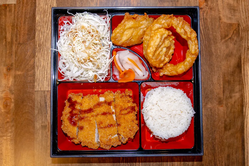 Bento box with sliced chicken katsu, rice, cabbage salad and fried squid rings