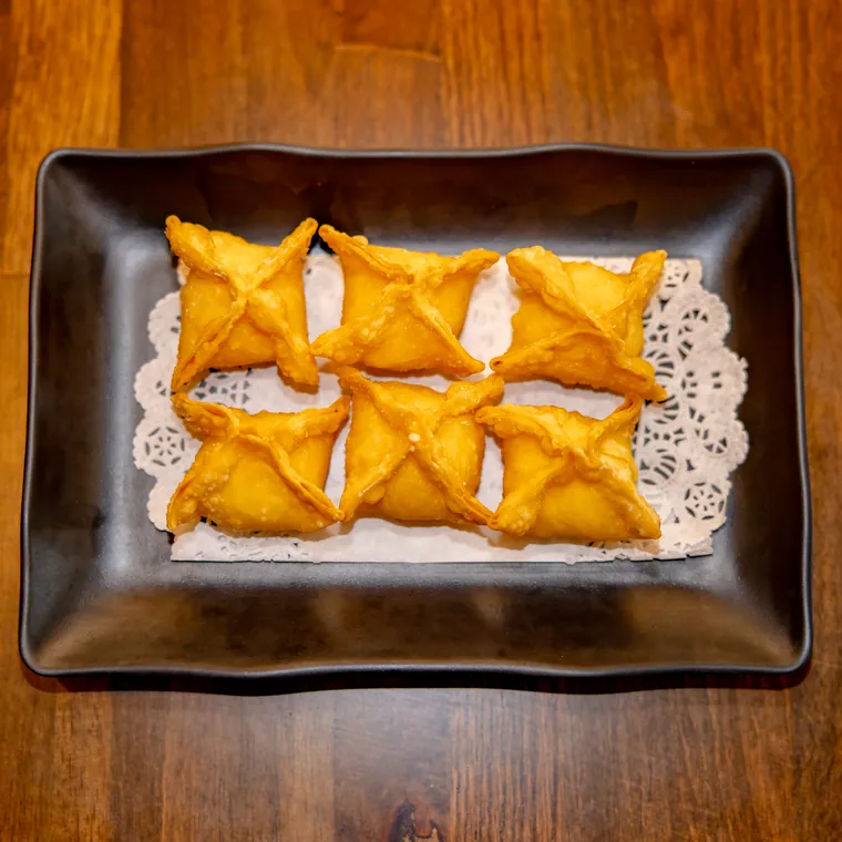 Six golden fried crab rangoon on a paper doily in a black dish