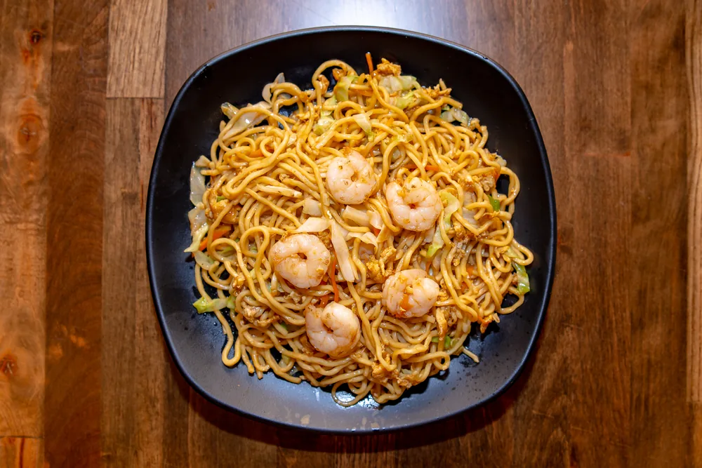 Yakisoba noodles with shrimp, cabbage, carrot and egg on a black plate