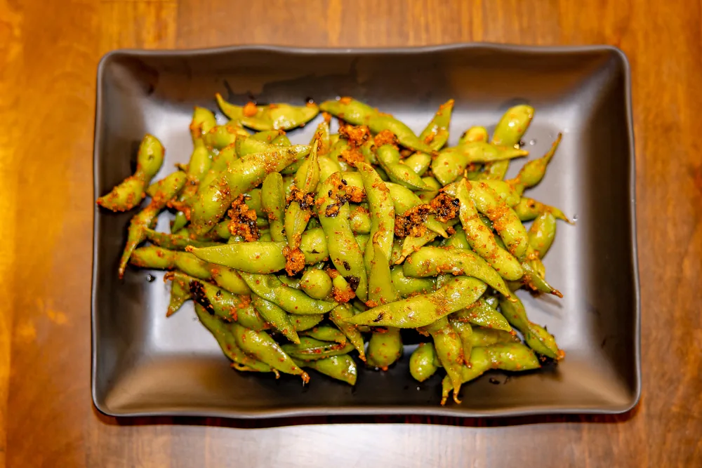 Edamame pods tossed in chili and garlic seasoning on a black plate