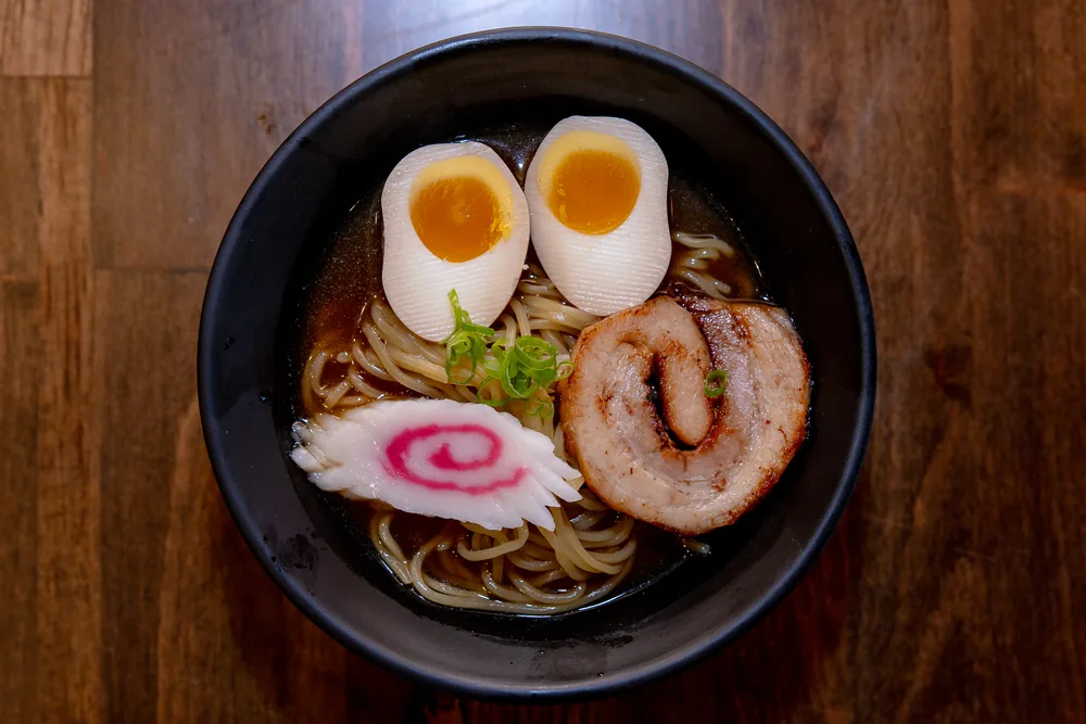 A small bowl of ramen with two egg halves, narutomaki and a slice of chashu pork