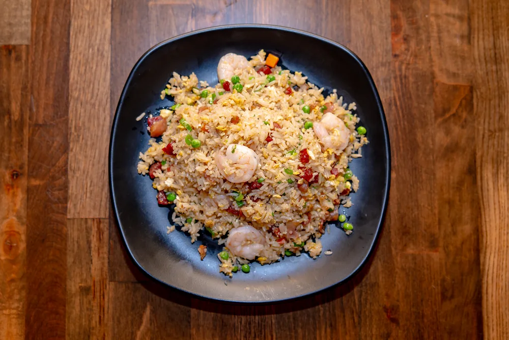 Fried rice with shrimp, Chinese sausage, peas and egg on a black plate