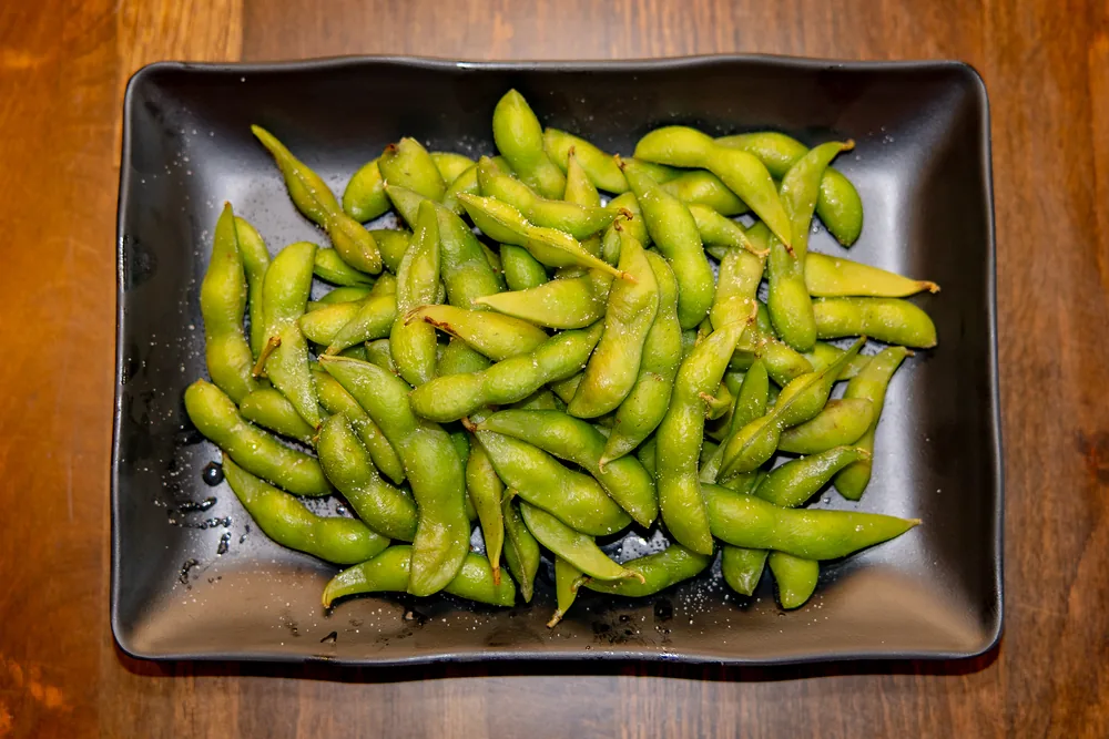 Salted edamame pods piled on a black plate