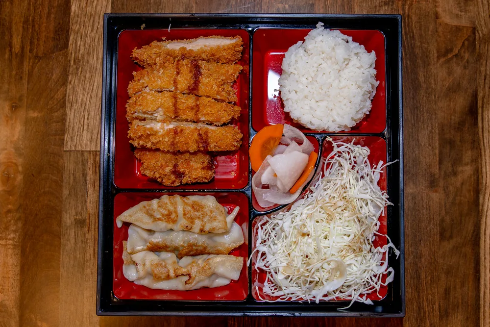 Bento box with sliced pork katsu, rice, gyoza and shredded cabbage