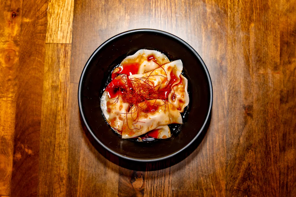 Wontons in chili oil topped with fried garlic and threads of red chili