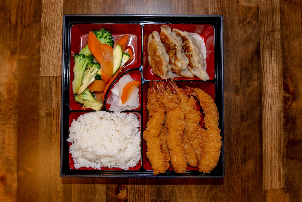 Bento box with fried shrimp, rice, gyoza and stir-fried vegetables