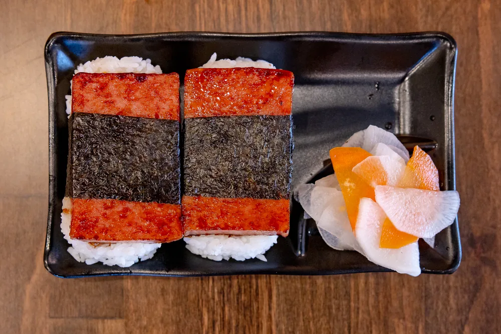 Two grilled spam musubi wrapped in nori, with pickled daikon and carrot