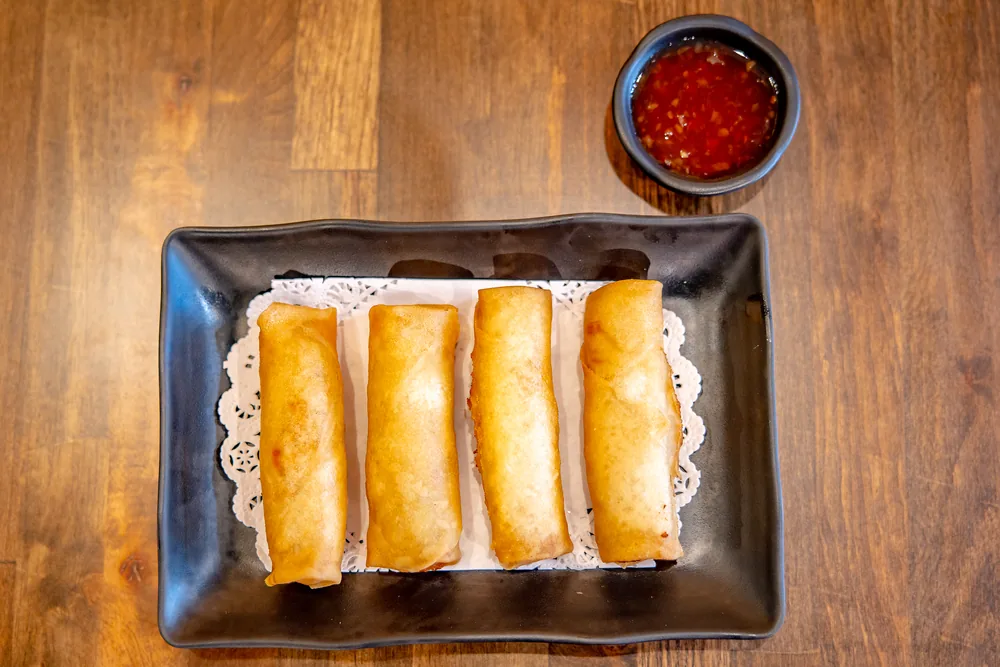 Four fried spring rolls on a paper doily with sweet chili dipping sauce