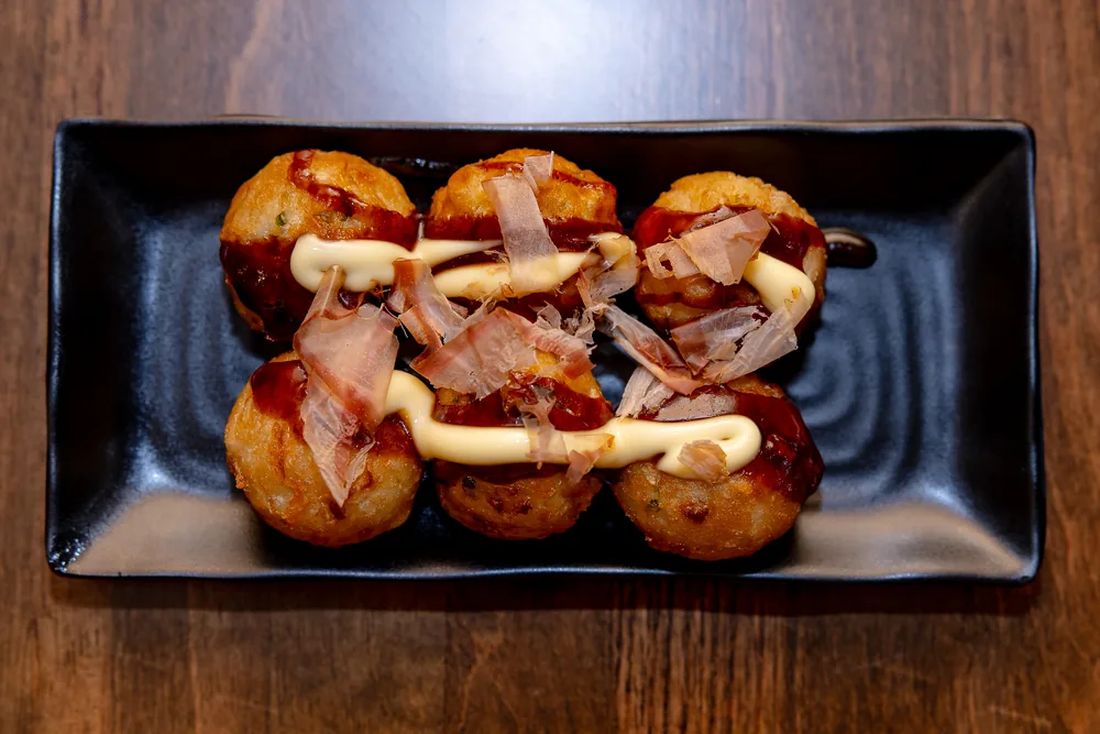 Six takoyaki drizzled with sauce and mayonnaise, topped with bonito flakes