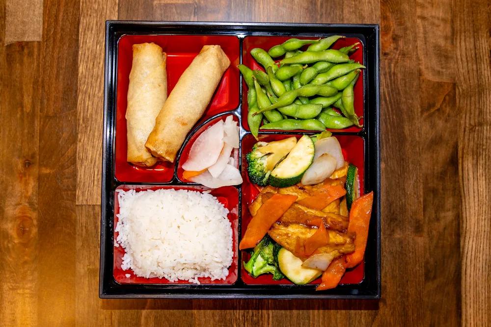 Bento box with tofu and vegetables, rice, spring rolls and edamame