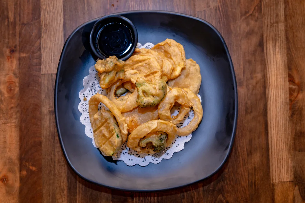 Assorted vegetable tempura on a paper doily with a bowl of dipping sauce